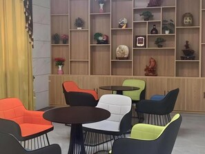 A seating area with multiple chairs and tables, a wooden wall with shelves containing various decorative items, and a curtain on the left.