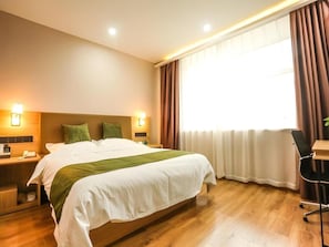 Ein Hotelzimmer mit einem großen Bett, Nachttischen, einem Schreibtisch und einem Fenster mit Vorhängen.