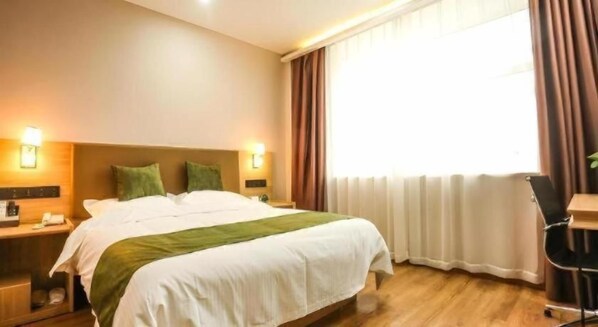Ein Hotelzimmer mit Bett, Nachttischen, Schreibtisch und einem fenster mit Vorhängen.