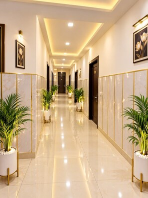 A hotel corridor with a polished floor, potted plants, framed artwork, and doors leading to rooms. - HOTEL GLOBAL REDIANCE DELHI AIRPORT  (New Delhi)
