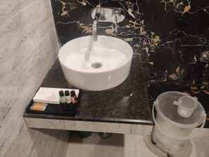A bathroom with a white sink, a marble-tiled wall, and a small shelf with toiletries. - HOTEL GLOBAL REDIANCE DELHI AIRPORT  (New Delhi)