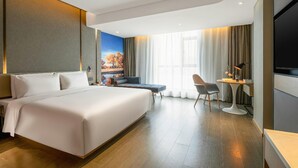 A hotel room with a large bed, a desk with a chair, a television, and a painting on the wall. - Atour Hotel (Lanzhou)