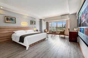 A hotel room with a large bed, a desk, a chair, a TV, and a view of a cityscape. - Shuiyang Nianhua Hotel (Chongqing)