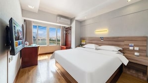 Habitación de hotel con una cama grande, un escritorio, un televisor y una ventana con vista a la ciudad.
