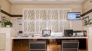 Un mostrador de recepción con dos monitores de computadora, una pantalla digital y un panel decorativo blanco.