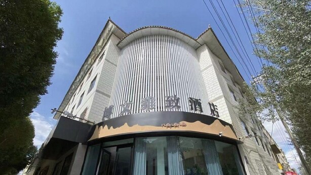 A hotel with a curved facade, large windows, and a sign with Chinese characters. - 7 Days Inn (Jiuquan)