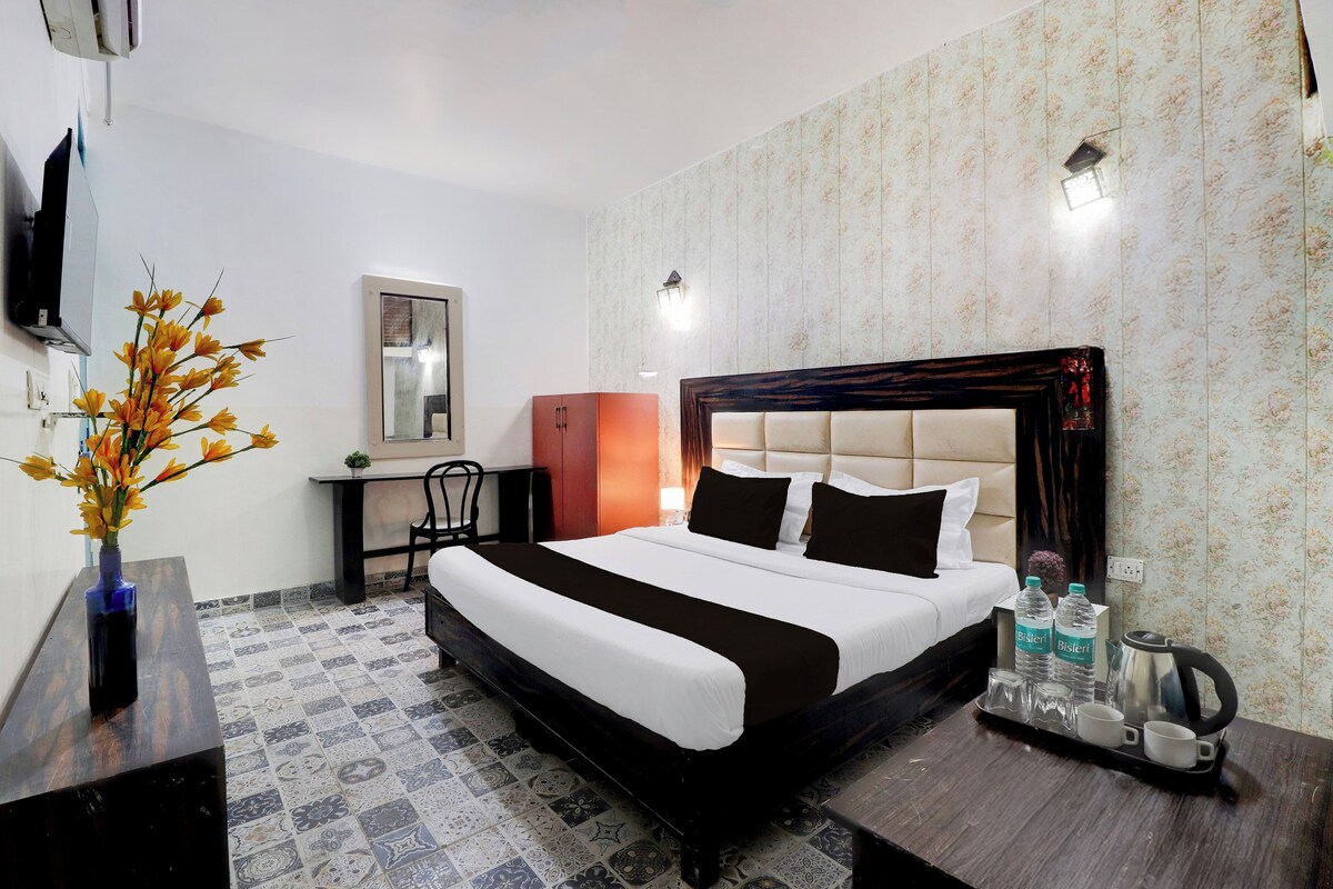 Habitación de hotel con una cama, un escritorio, una silla, un televisor y un florero con flores.