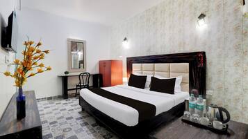 Habitación de hotel con una cama, un escritorio, una silla, un televisor y un florero con flores.