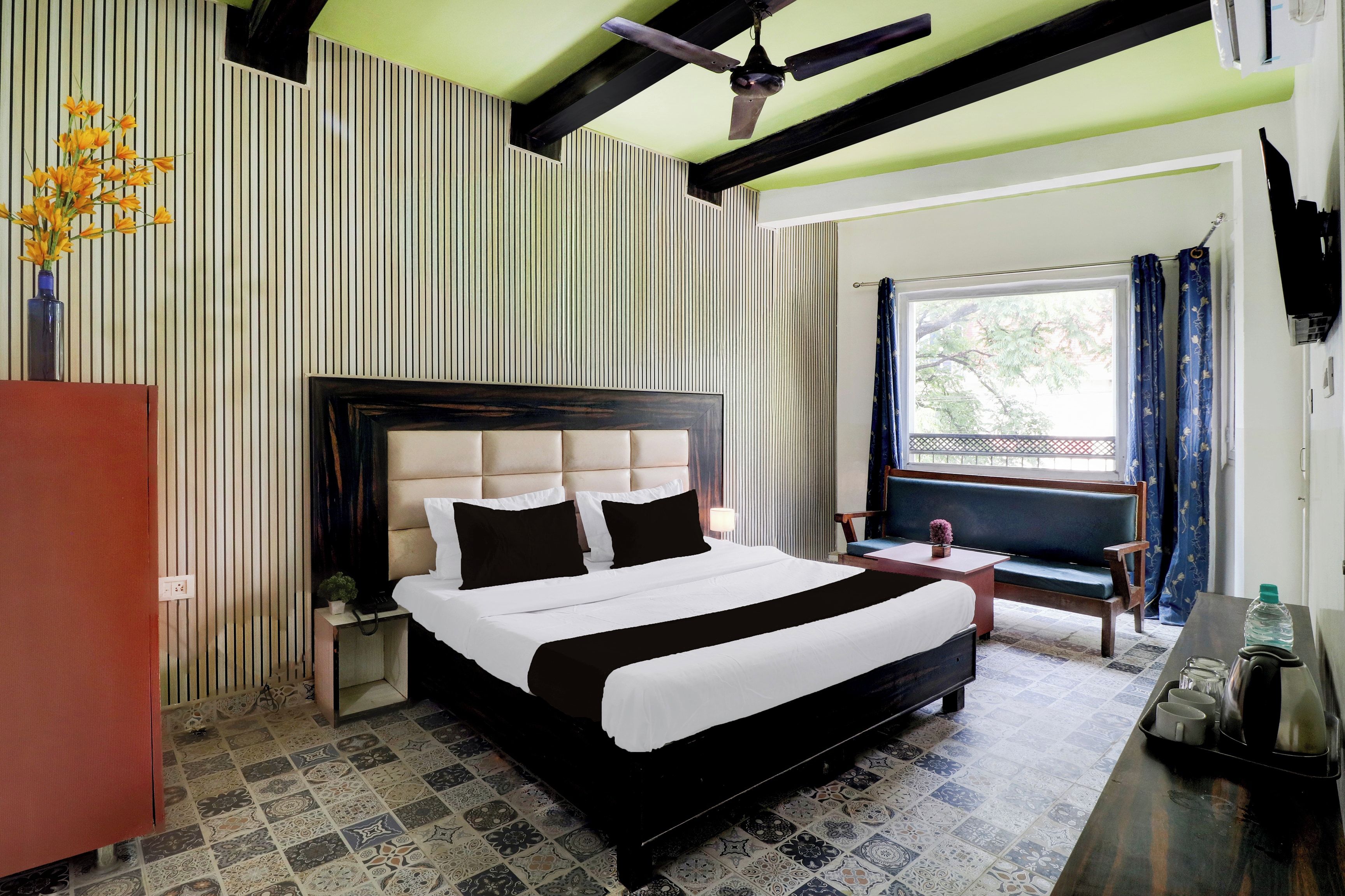 Habitación de hotel con una cama grande, un escritorio, una silla, una ventana con cortinas y un ventilador de techo.