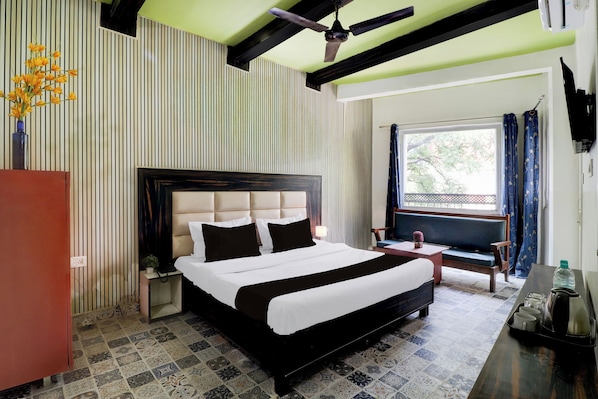 A hotel room with a large bed, a desk, a chair, a window with curtains, and a ceiling fan.