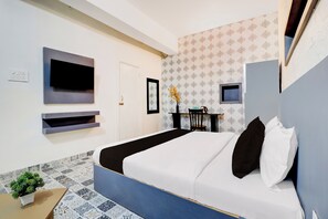 Una habitación de hotel moderna con una cama, un televisor de pantalla plana montado en la pared, un escritorio pequeño con una silla y una planta en maceta.