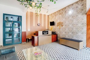 Zona de recepción de hotel con mostrador, un reloj, televisor en la pared y piso estampado.