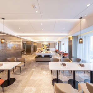 A modern hotel lobby with a central seating area, a reception desk, and a view of the dining area. - Beijing Road Atour Hotel (Linyi)