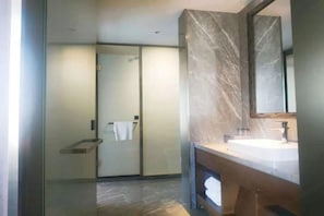 Un baño moderno con cabina de ducha de vidrio, encimera de mármol y un espejo grande.