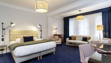 Une chambre d’hôtel avec un grand lit, un canapé, un fauteuil, un bureau et deux lampes suspendues.