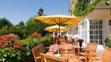 Un espace extérieur aménagé avec des tables et des chaises en bois, des parasols jaunes et un bâtiment blanc doté de fenêtres.