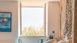 A bedroom with a bed, a nightstand, a lamp, and a window with a view of trees. - Vrbo Property (Limoux)