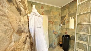 Un bagno con una parete in pietra, un asciugamano bianco appeso a un gancio e uno spazio doccia con porta in vetro.