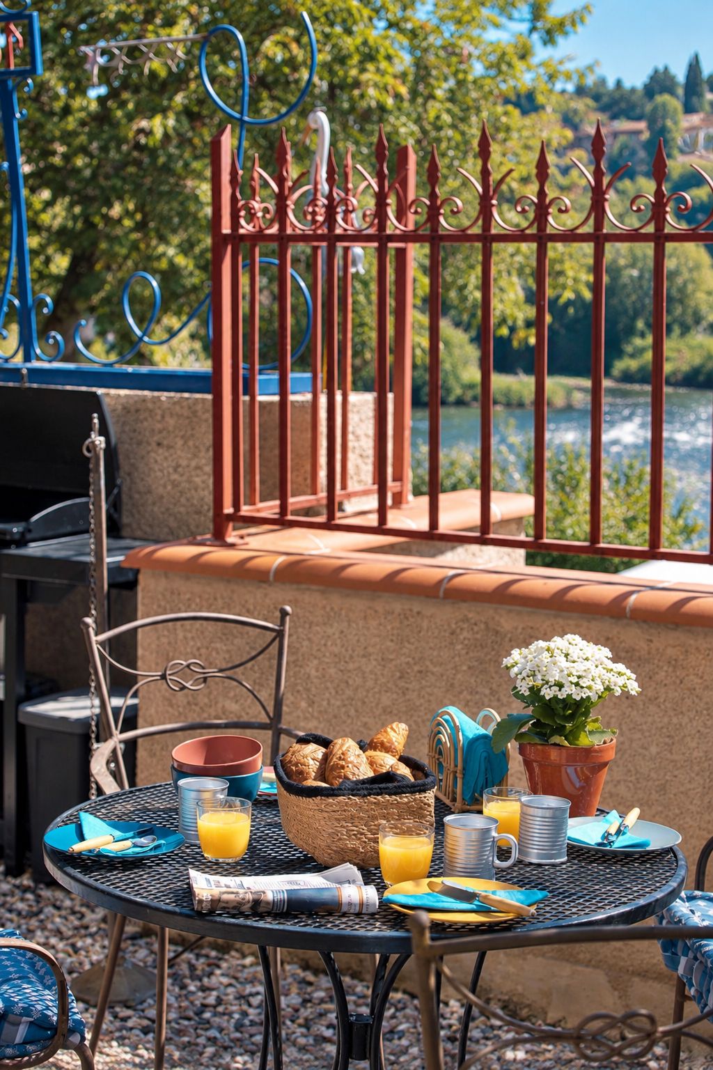 Un área de comedor al aire libre con una mesa dispuesta para el desayuno, que incluye croissants, jugo de naranja y un florero.