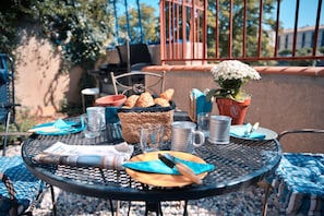 Une table ronde en métal, sur laquelle se trouvent un panier de croissants, une plante en pot et un journal.