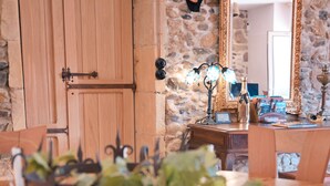 A wooden dining table with chairs, a stone wall, a wooden cabinet, and a mirror with an ornate frame. - Vrbo Property (Limoux)