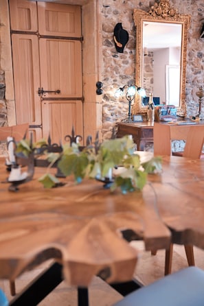 Une table de salle à manger en bois, des chaises, un mur en pierre, un buffet en bois et un miroir avec un cadre orné.