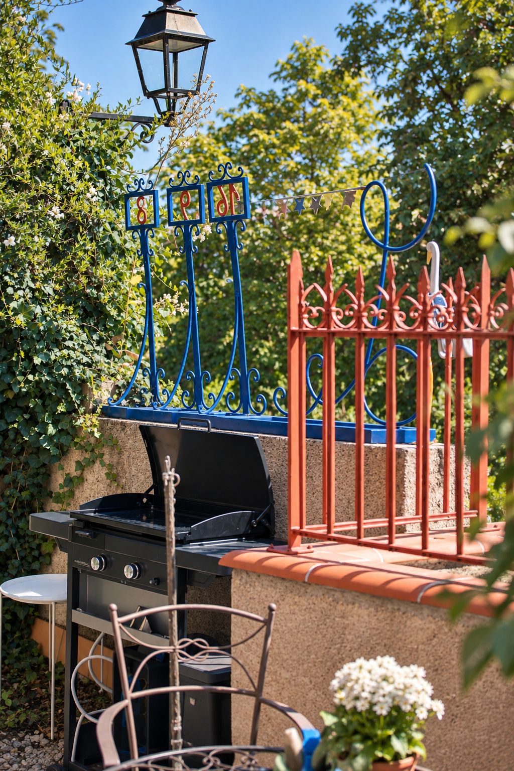 Una griglia da barbecue con un recinto decorativo blu e rosso, un lampione e vegetazione lussureggiante sullo sfondo.