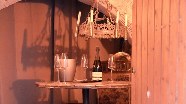A rustic wooden interior with a table set for dining, two stools, and a wine bottle. - Vrbo Property (Limoux)