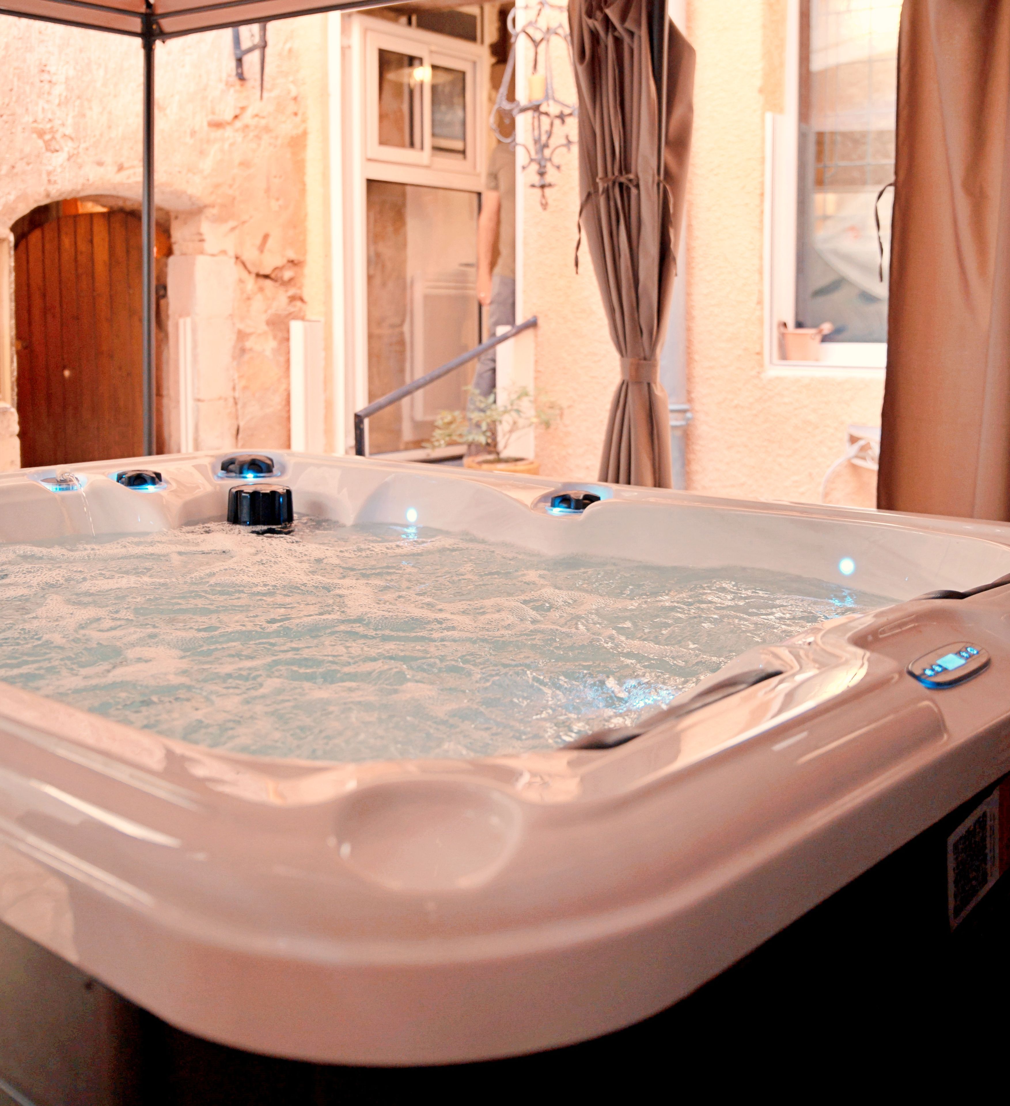 A hot tub with multiple jets, a wooden door, and a window with curtains.