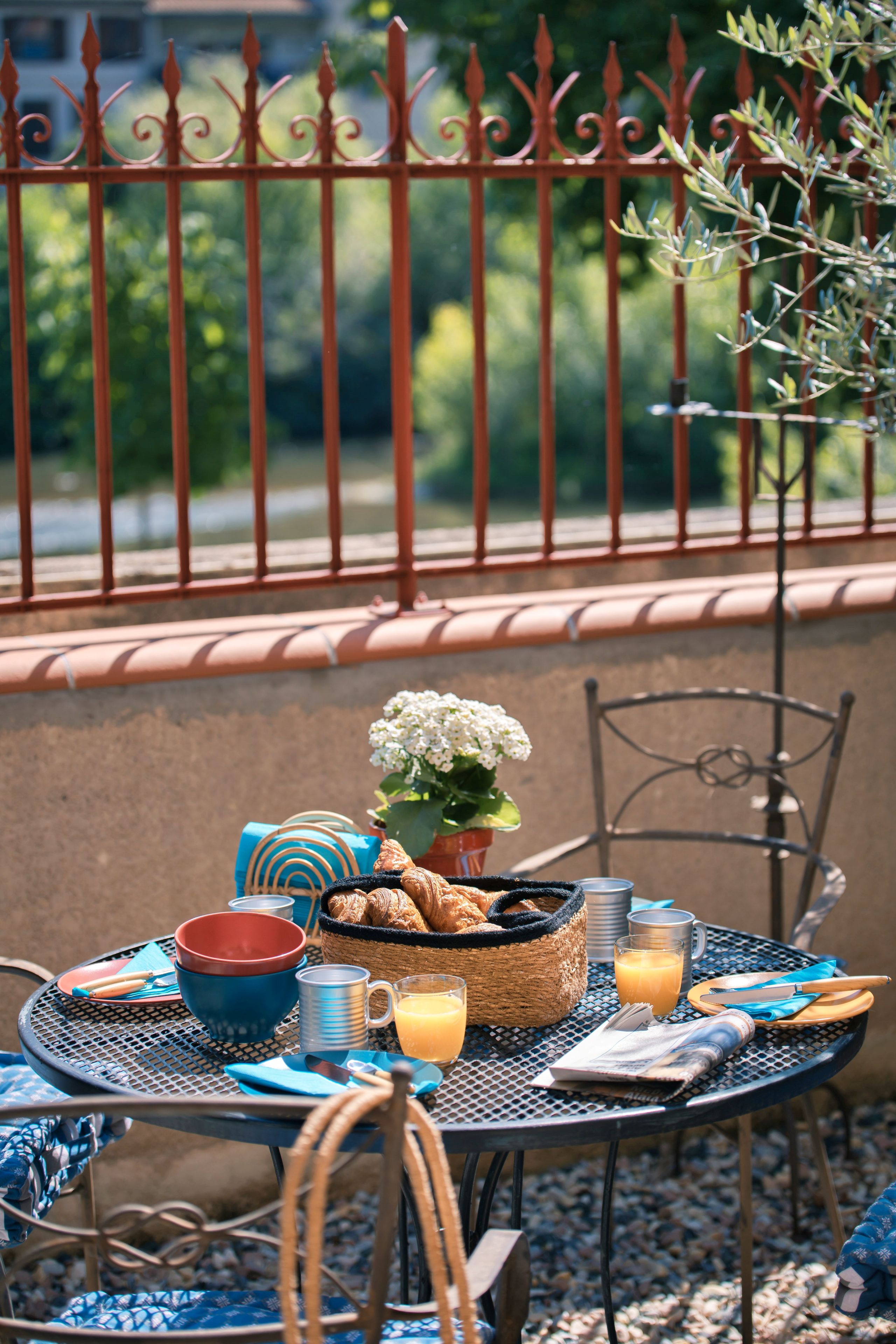 A round metal table with breakfast items, a wicker basket, and a potted plant.