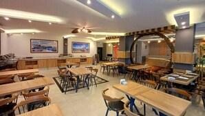 Un interior de restaurante moderno con mesas y sillas de madera, un área de estar central y un elemento decorativo en la pared.
