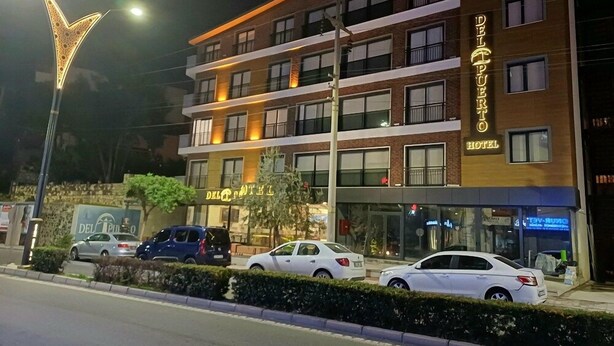 Un hotel de varios pisos con un letrero llamativo, múltiples balcones y coches estacionados en la entrada.