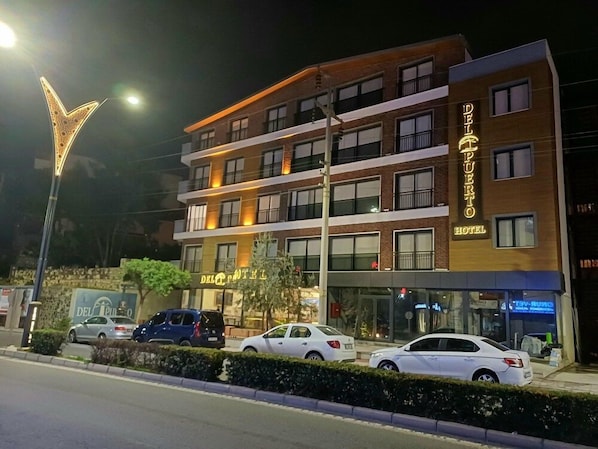 Un hotel de varios pisos con un letrero llamativo, múltiples balcones y coches estacionados en la entrada.