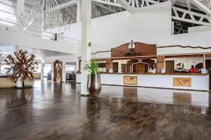 Un vestíbulo espacioso con un mostrador de recepción de madera, una planta ornamental grande y un candelabro moderno.