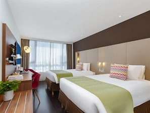 A hotel room with two beds, a desk, a chair, and a large window with curtains.