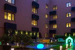 A multi-story building with balconies, outdoor seating, and illuminated windows.