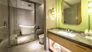 Et moderne badeværelse med bruseniche, et fristående badekar, et toiletbord med vask og et stort spejl med lys.