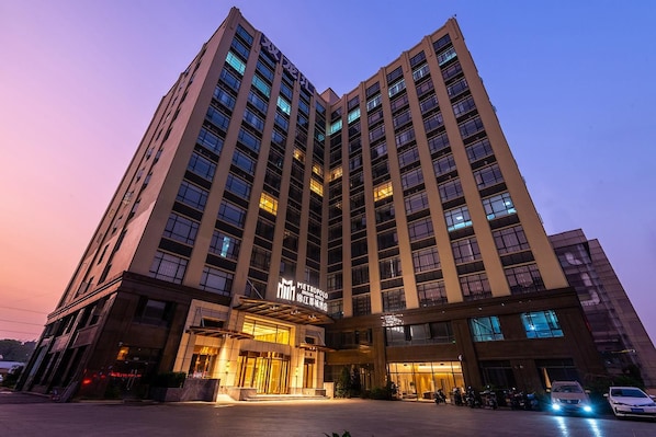 Un hôtel de grande hauteur, avec de nombreux étages, une entrée imposante et une façade bien éclairée.