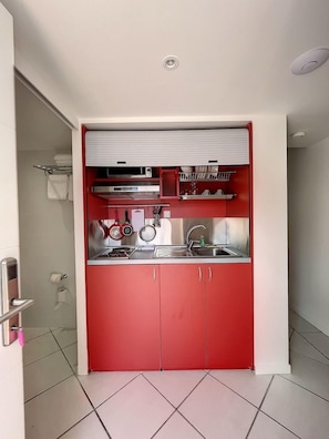 A compact kitchen with red cabinets, a stainless steel sink, and a built-in oven. - Anse Marcel Beach Resort (Anse Marcel)