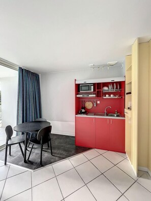 Cocina compacta con comedor, que incluye microondas, lavamanos y armarios rojos.