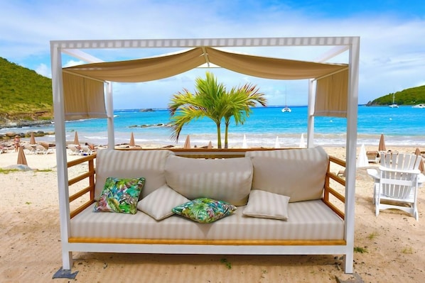 A beachside bed with a canopy, white cushions, and a tropical pillow. - Anse Marcel Beach Resort (Anse Marcel)