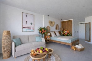 Una sala de estar moderna con un sofá, una cama, una mesa de centro con fruta y un jarrón grande de flores.