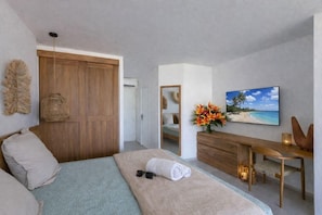 A modern bedroom with a large bed, a wooden wardrobe, a desk with a chair, a television, and a beach-themed painting. - Anse Marcel Beach Resort (Anse Marcel)