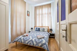 Una camera da letto con un letto, un comodino, una lampada e una finestra con tende.