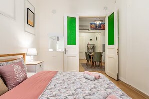 Una camera da letto con un letto, un comodino, una lampada, uno specchio e una porta che dà su una zona pranzo con tavolo e sedie.