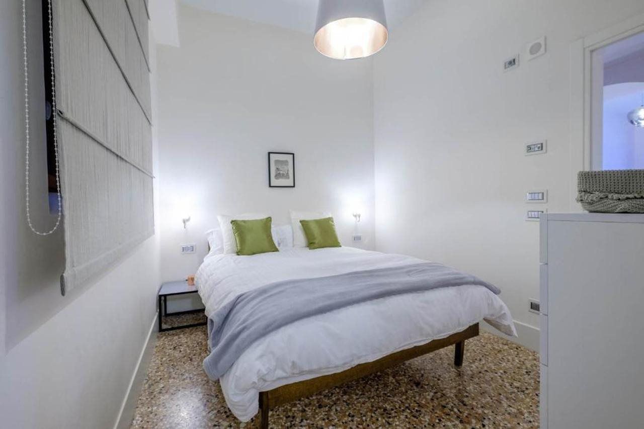 A bedroom with a bed, bedside lamps, a small bedside table, and a wall-mounted radiator.