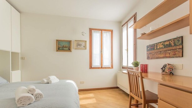 A bedroom with a bed, a desk, and a chair. There are two windows, one with a view of the outside and another with a view of the interior. - Venezia - Castello 1542 (Venice)