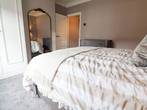 A bedroom with a large bed, a dresser, a mirror, and a door leading to another room. - 9 North Street (Chester)