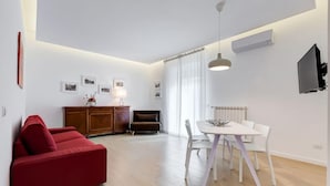 A modern living room with a red sofa, a dining table with chairs, a cabinet, and a television mounted on the wall. - Lovely 3 Rooms Apartment Close Trastevere Station (Rome)