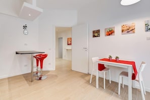 A modern kitchen with a dining area, featuring a white table with red chairs, a red bar stool, and wall-mounted pictures.